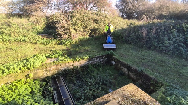Image of a person driving a machine that is cutting vegetation around a concrete tank